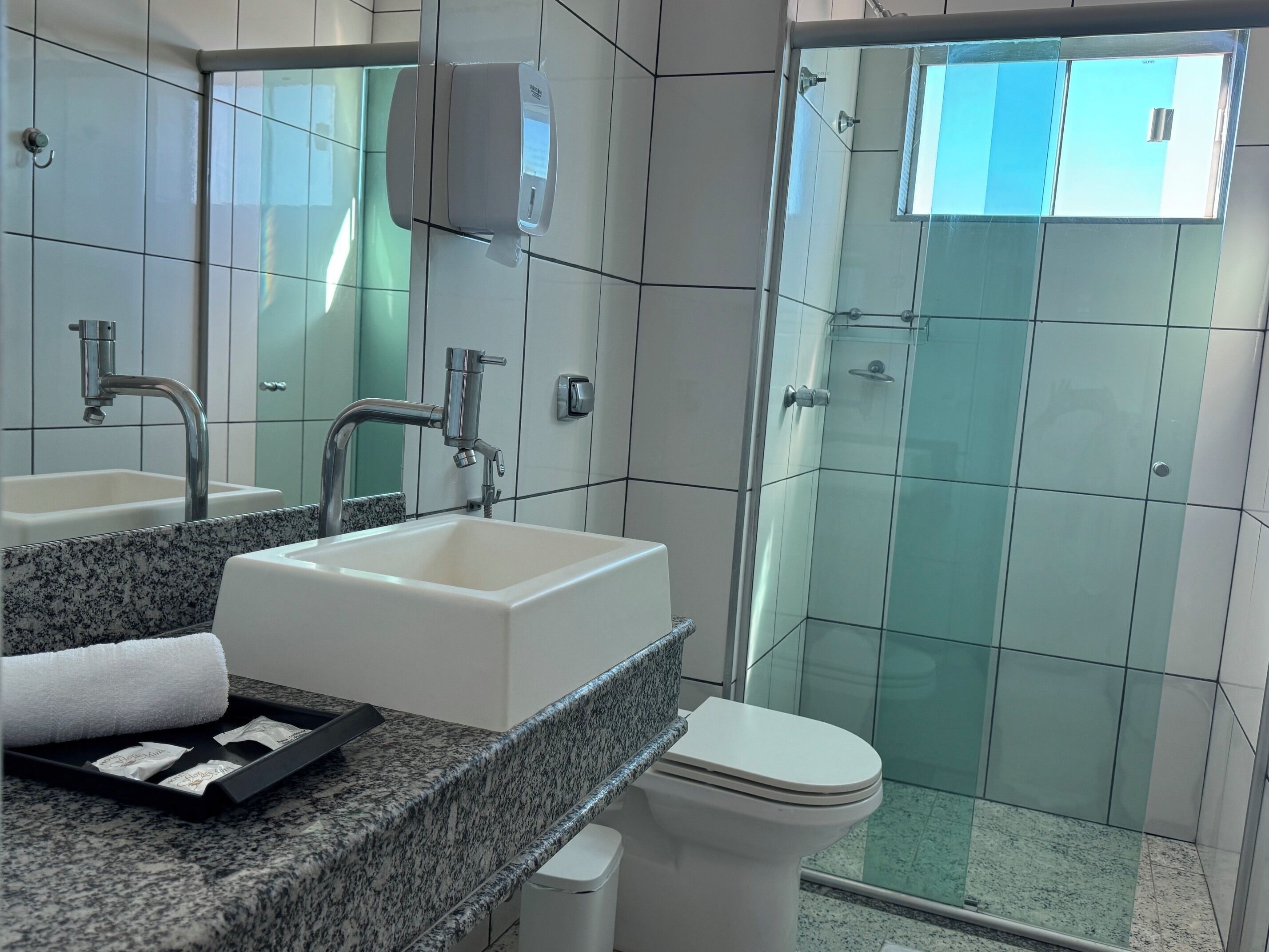Un bagno moderno con piano in granito, lavandino bianco, specchio, box doccia in vetro e un water.