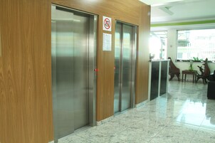 Un ascensor moderno con paneles de madera, un cartel de prohibido fumar y un aviso en la pared.