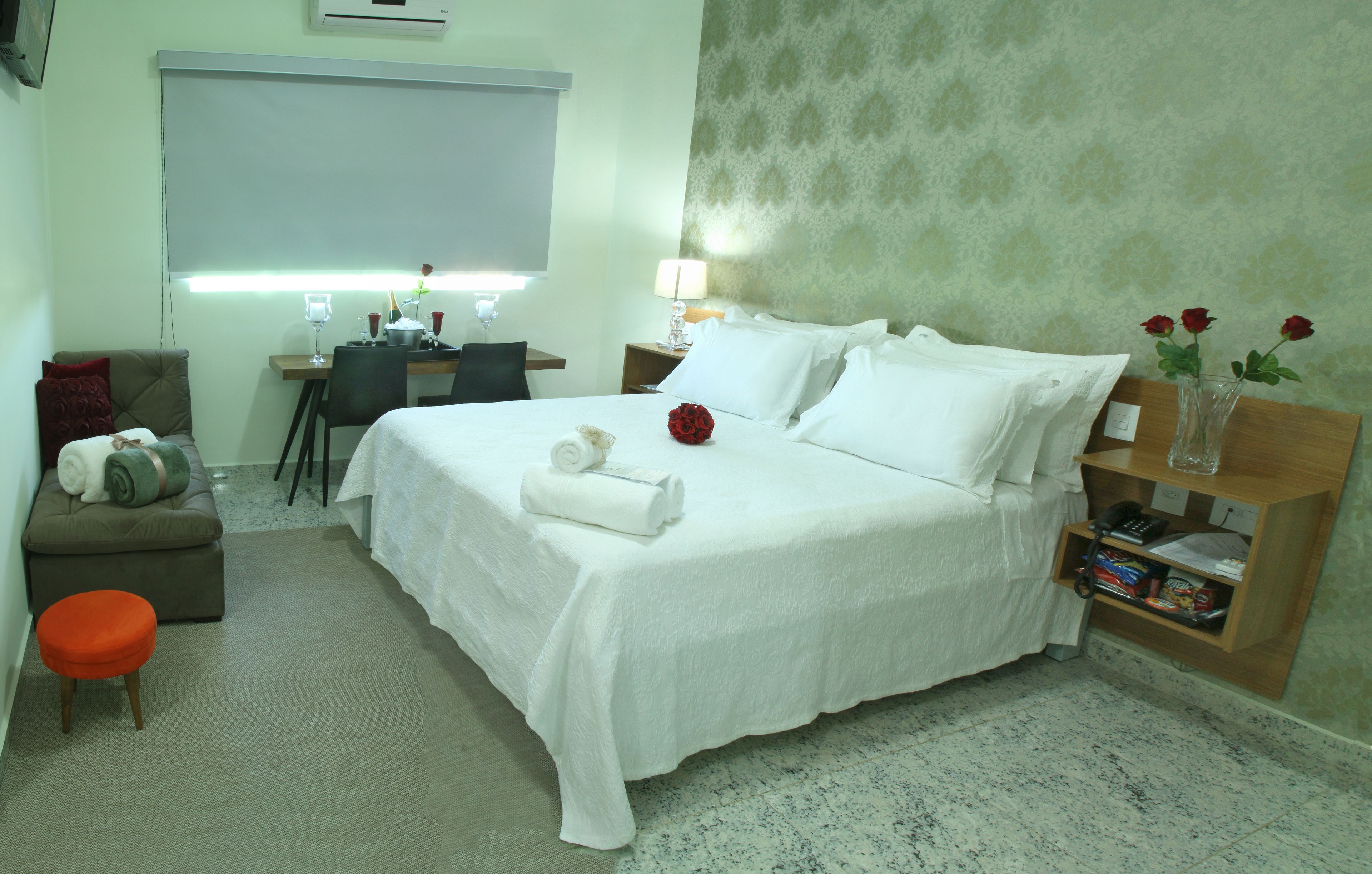 A neatly arranged hotel room with a bed, a desk, a chair, a small table, and a nightstand.