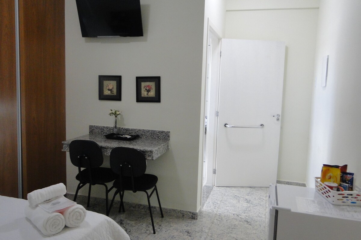 A hotel room with a bed, a desk with two chairs, a TV mounted on the wall, and a door.