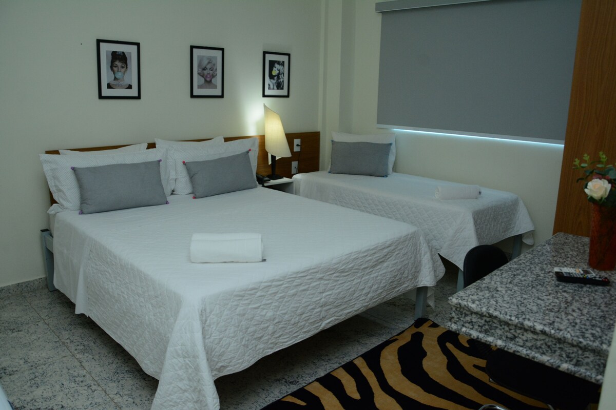 A hotel room with two beds, a desk, a chair, a zebra-patterned rug, and framed pictures on the wall.