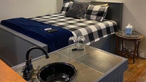 A modern bedroom with a checkered bedspread, a blue blanket, a bedside table with a tissue box, and a wall-mounted heater. - Hall House Hotel (Dahlonega)