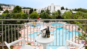 A balcony with white chairs and a table with a bottle and glasses, overlooking a pool area with lounge chairs and a hot tub. - Hotel Laguna Garden (Albena)