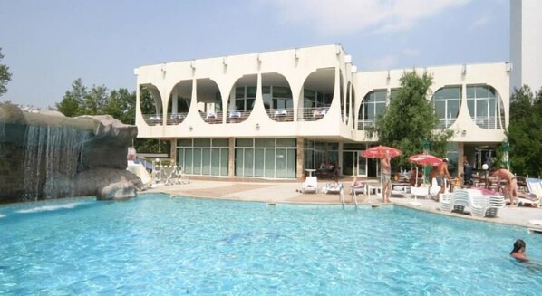 A pool area with a waterfall feature, lounge chairs, and umbrellas. - Hotel Laguna Garden (Albena)