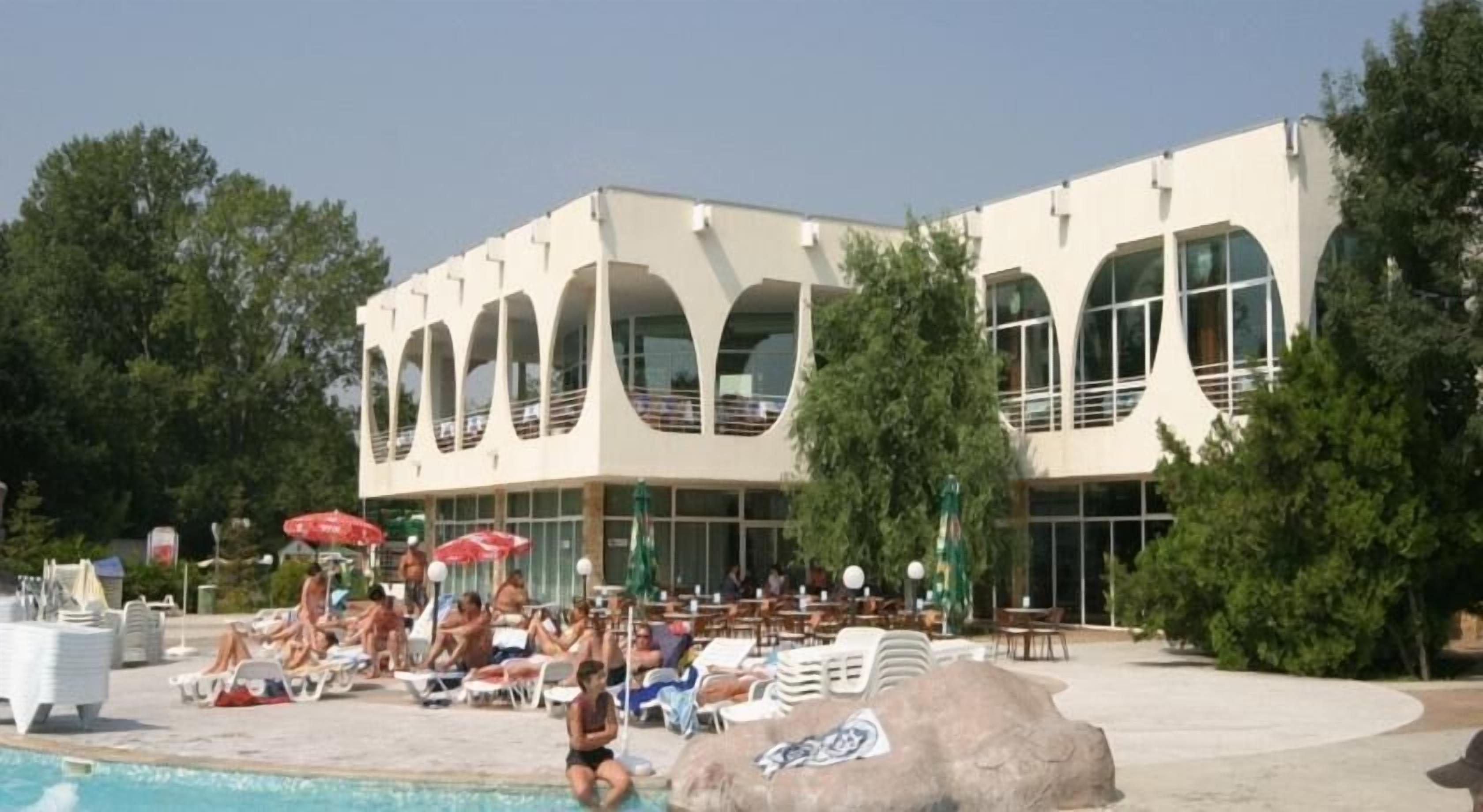 Un bâtiment moderne doté de grandes fenêtres et d’un espace piscine avec des chaises longues et des parasols.