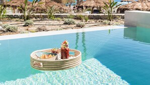 Ein Pool mit einer schwimmenden Bar, Palmen und im Hintergrund Strohschirmen.