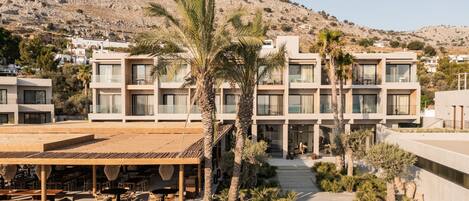 A modern hotel with a courtyard, palm trees, and a view of a hilly landscape.
