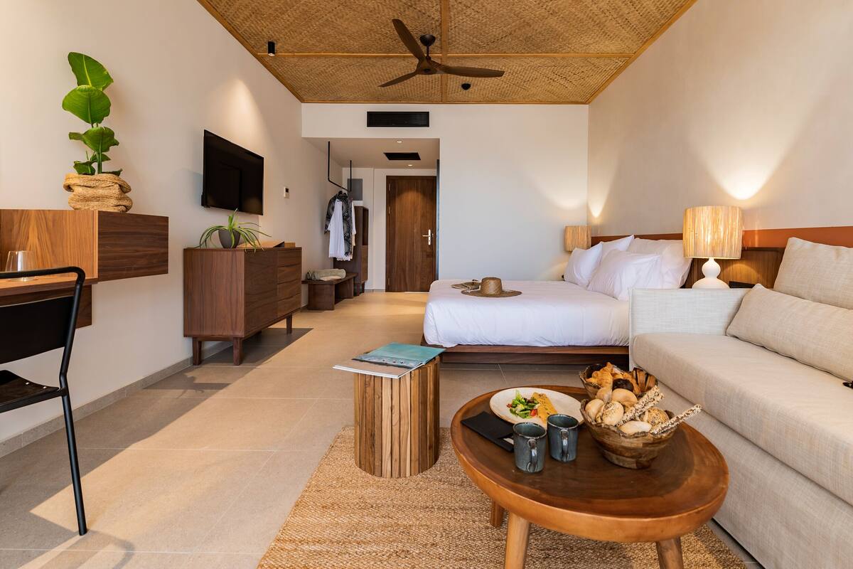 A modern hotel room with a bed, sofa, wooden coffee table, and a TV on the wall.