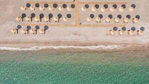 Eine Luftaufnahme eines Strandes mit in Reih und Glied angeordneten Liegestühlen und Sonnenschirmen.
