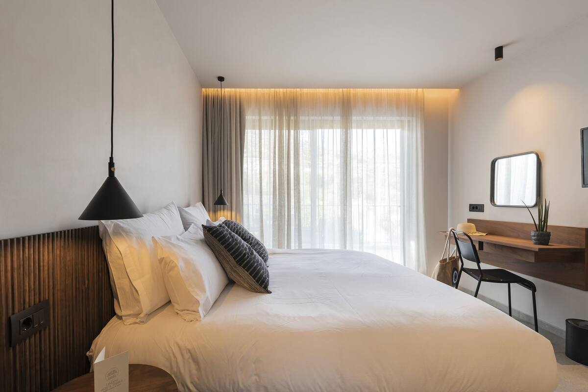 A modern hotel room with a large bed, a desk, and a chair.
