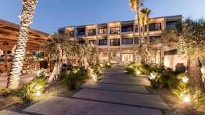 Ein mehrstöckiges Hotel mit modernem Design, das einen zentralen Innenhof mit Palmen und einem gepflasterten Wegzug bietet.