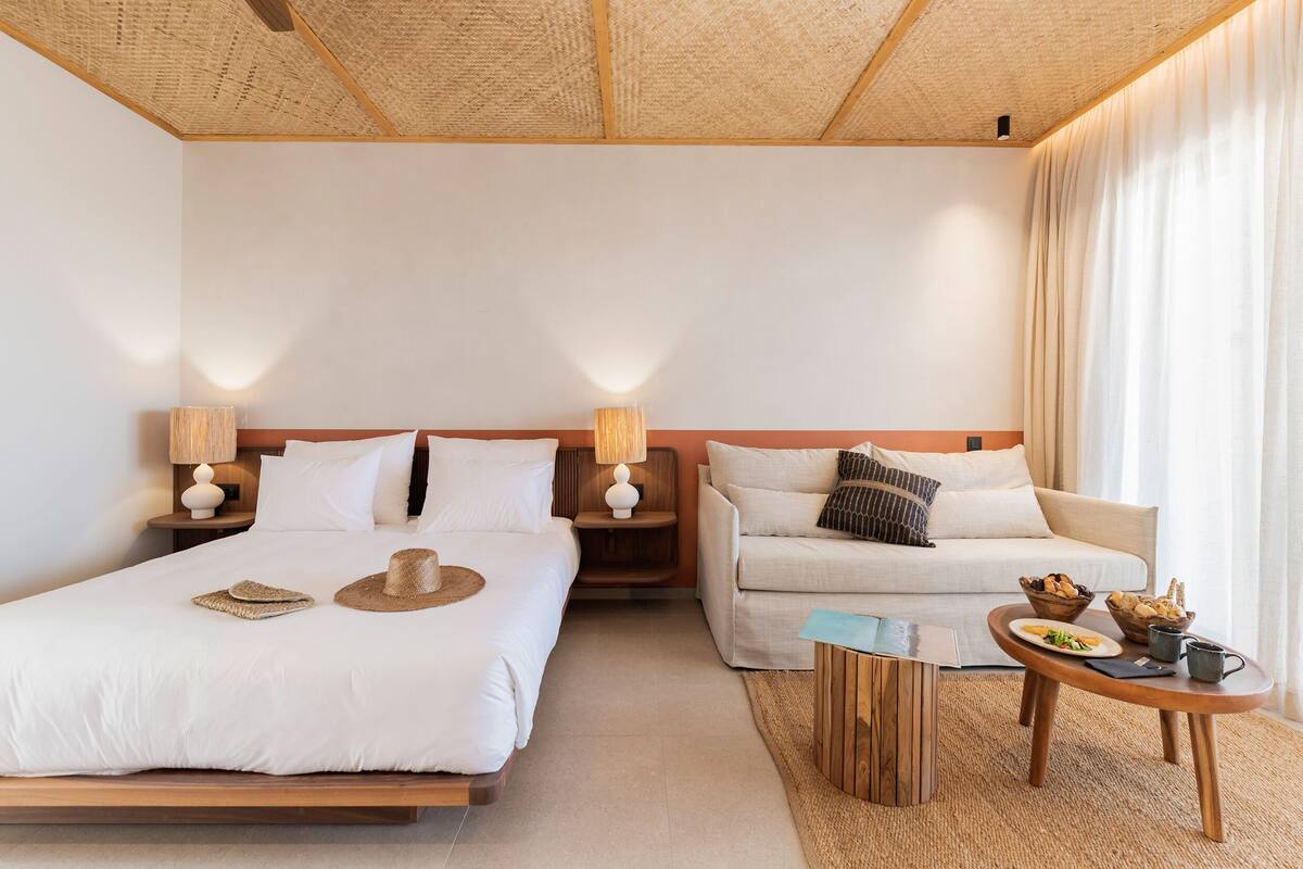 A hotel room with a large bed, a sofa, a small table with food, and two bedside lamps.