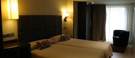 A hotel room with two beds, a desk, a chair, and a window with curtains.