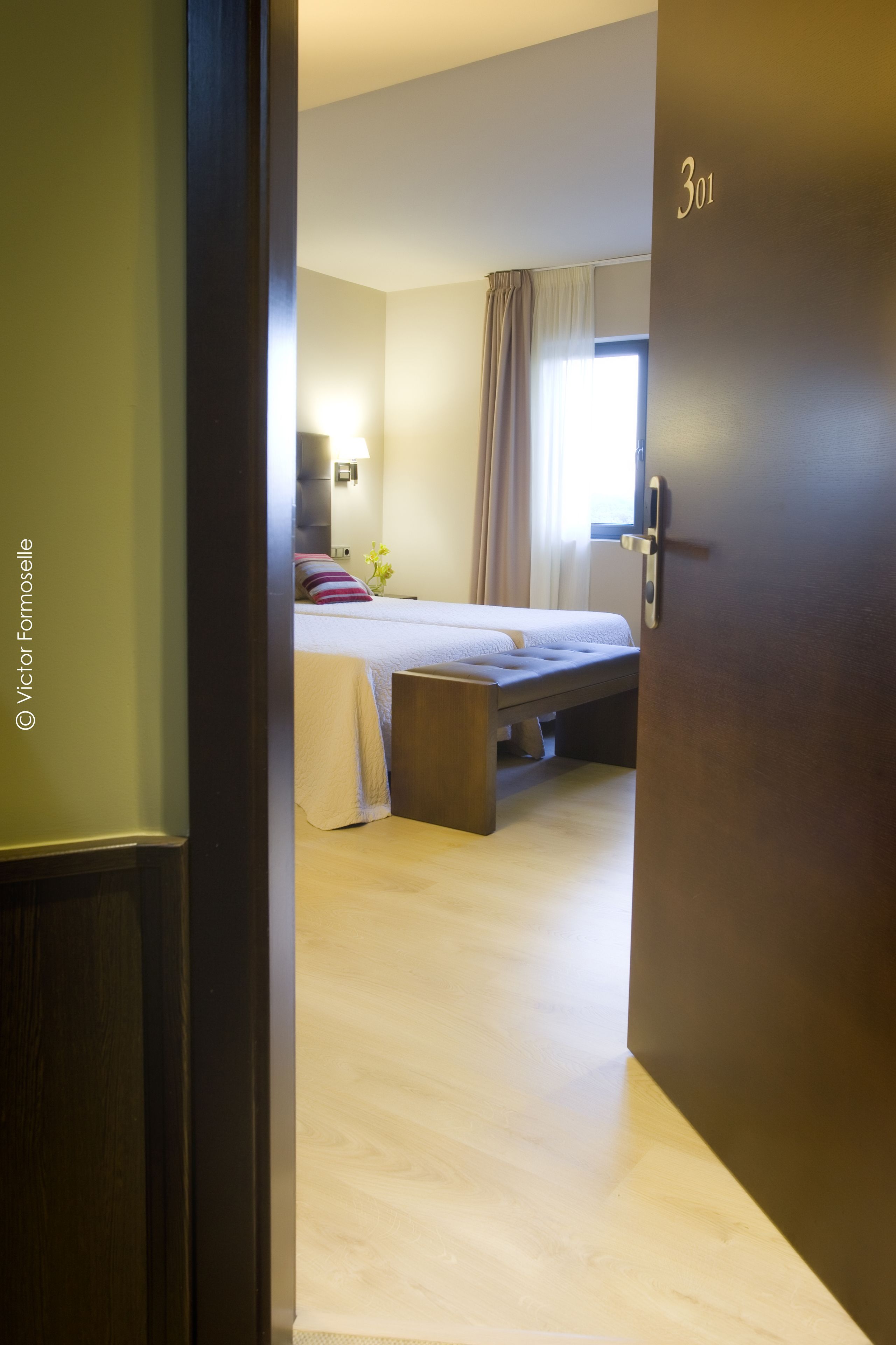 Habitación de hotel con una cama, una mesita de noche, una ventana con cortinas y una puerta con el número 301.