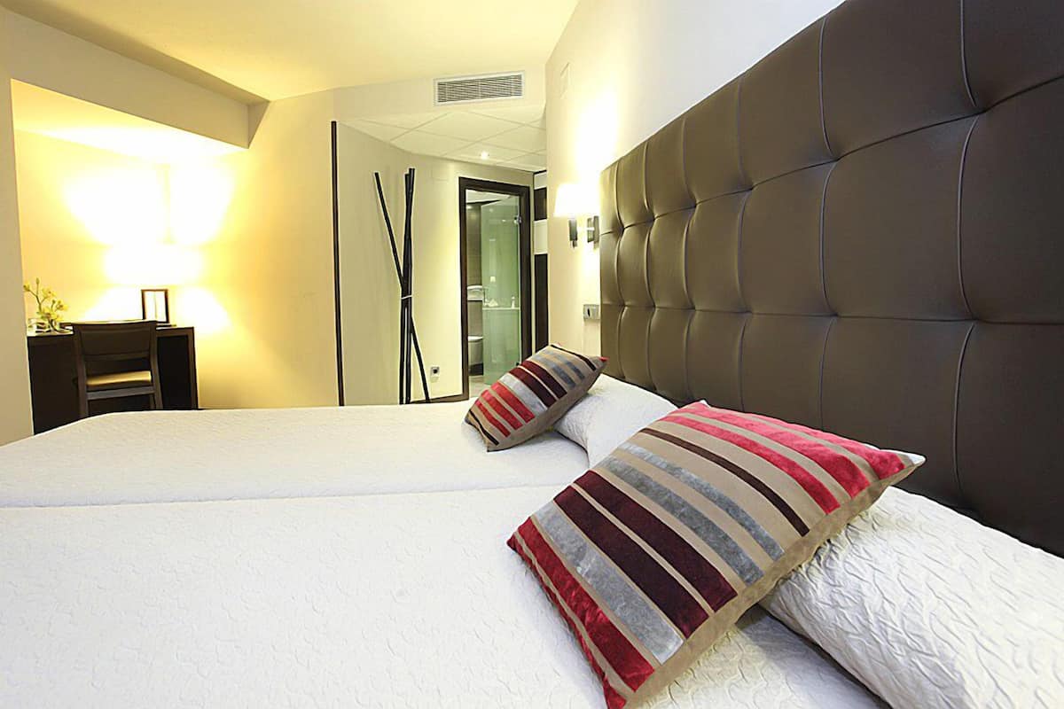 A hotel room with a large bed, two pillows, a bedside table, a lamp, and a mirror.