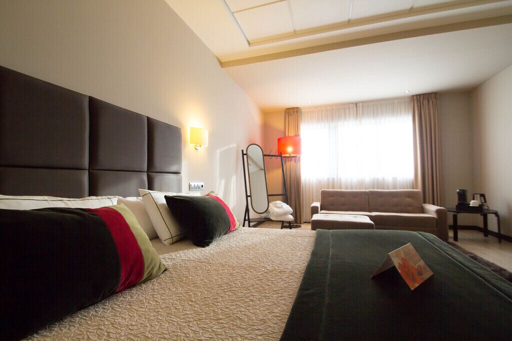 Habitación de hotel con una cama grande, un sofá, un escritorio y una ventana con cortinas.