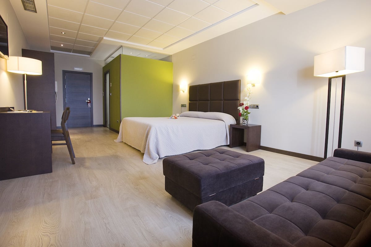 A hotel room with a bed, a sitting area, a desk, and a green accent wall.