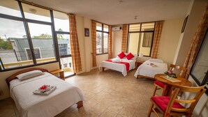 A hotel room with two beds, a dining table with chairs, and large windows with curtains. - Hotel Red Booby (Puerto Ayora)