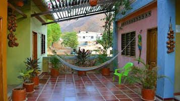 A covered patio with a hammock, potted plants, and a view of a mountain.