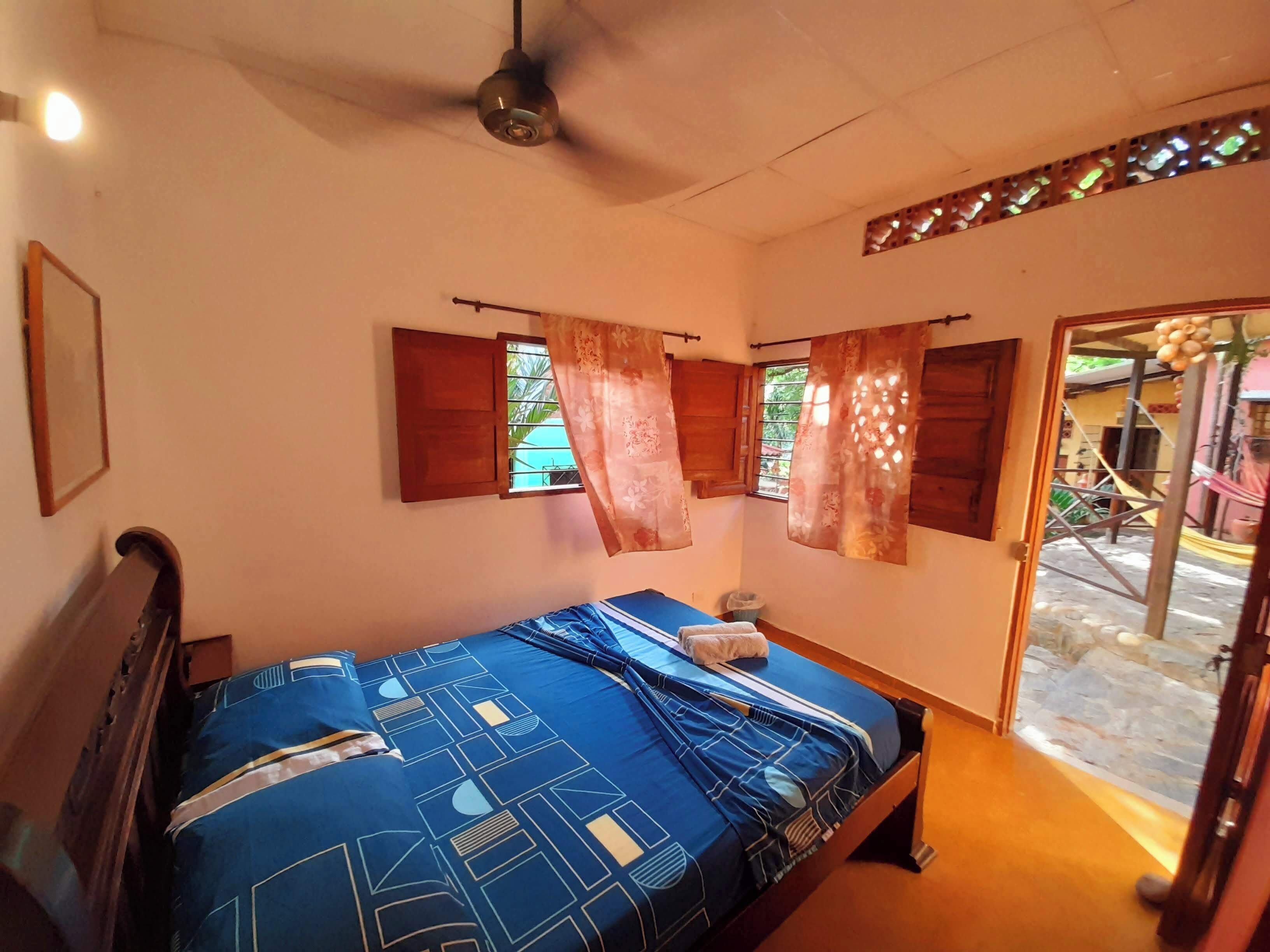Quarto com cama, ventoinha no teto e janela com cortinas.
