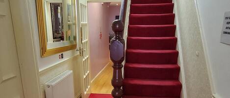 A hallway with red carpet leading to a staircase with a handrail.