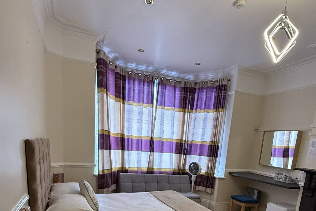 A bedroom with a bed, bedside table, chair, desk, and a mirror.