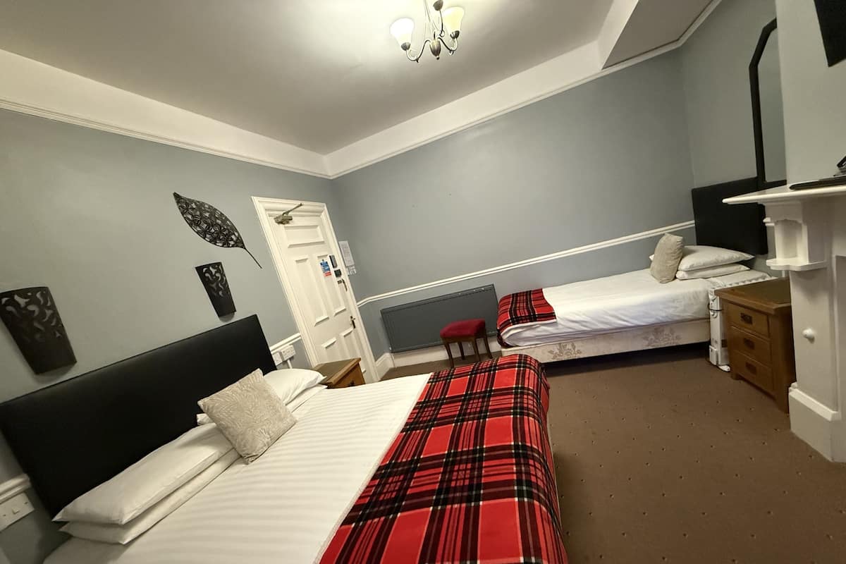 A bedroom with two beds, a dresser, a chair, and a radiator.