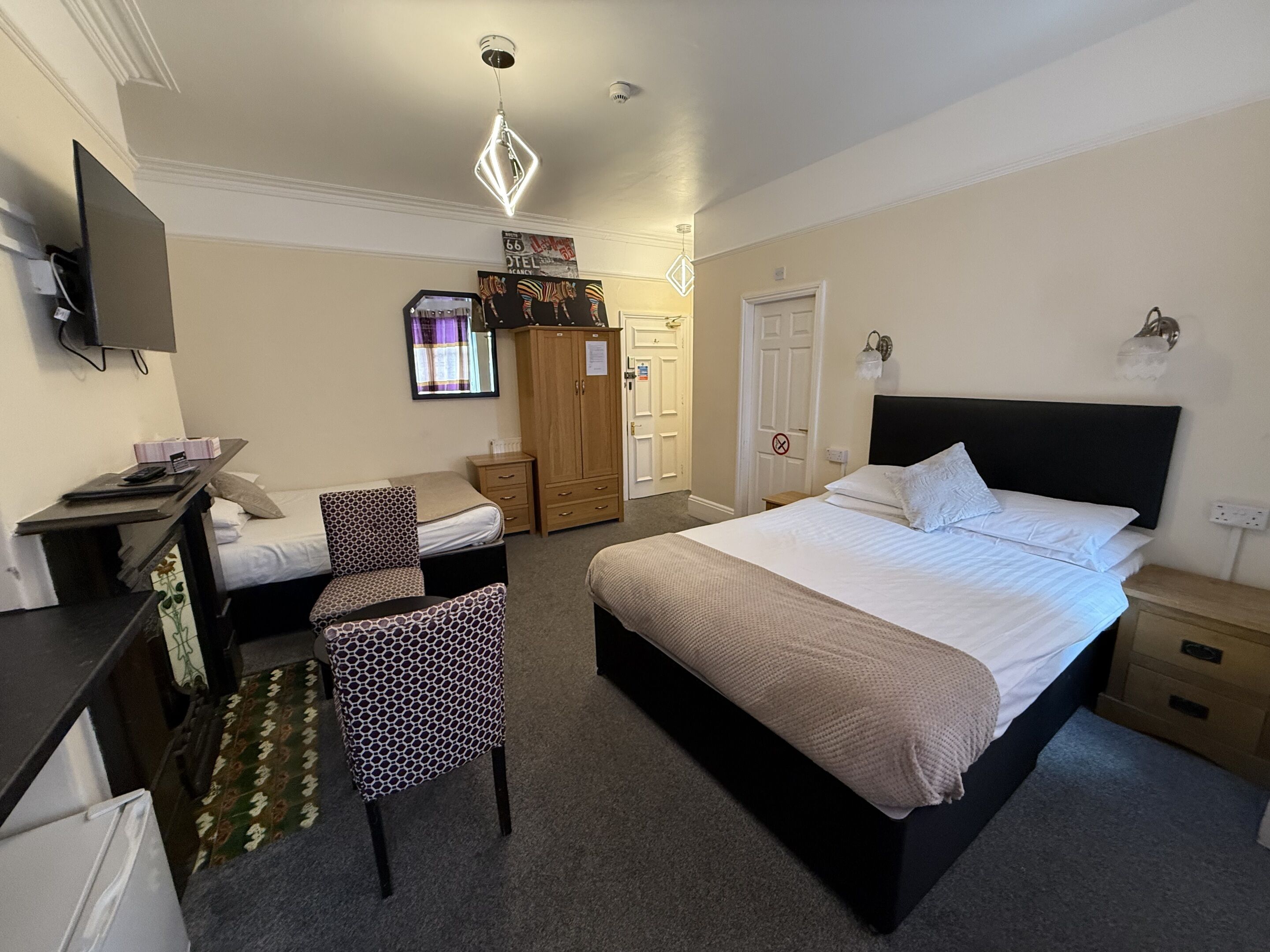 A bedroom with a bed, a desk, a chair, a wardrobe, and a television.