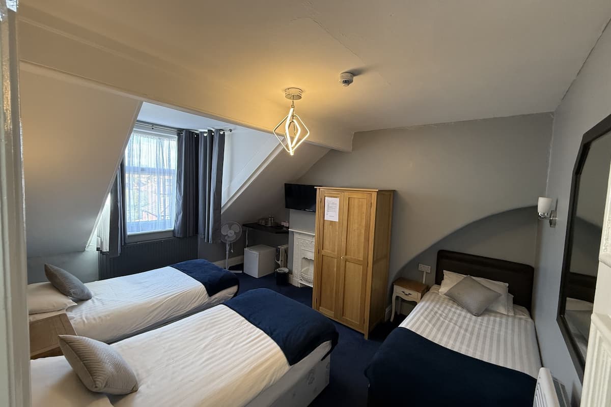 A room with two beds, a wardrobe, a desk, a chair, a television, and a window with curtains.