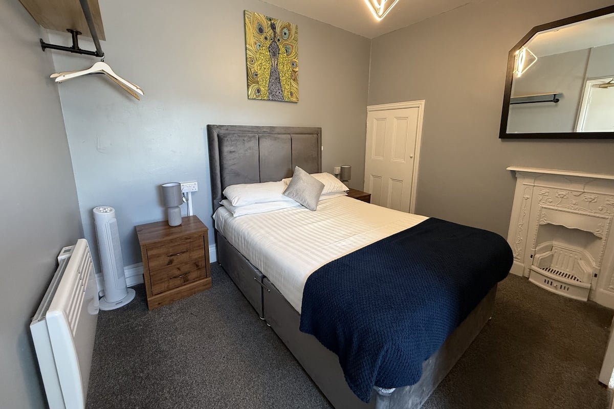 A bedroom with a bed, a nightstand, a radiator, a heater, a mirror, and a fireplace.