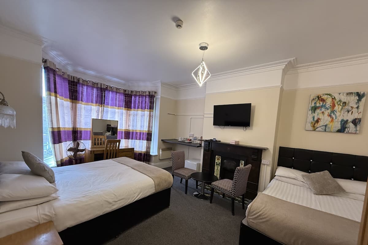 A hotel room with two beds, a desk, a chair, a TV, and a fireplace.