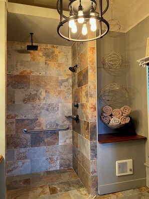 A shower with stone tiles, a towel rack, and a ceiling light fixture.