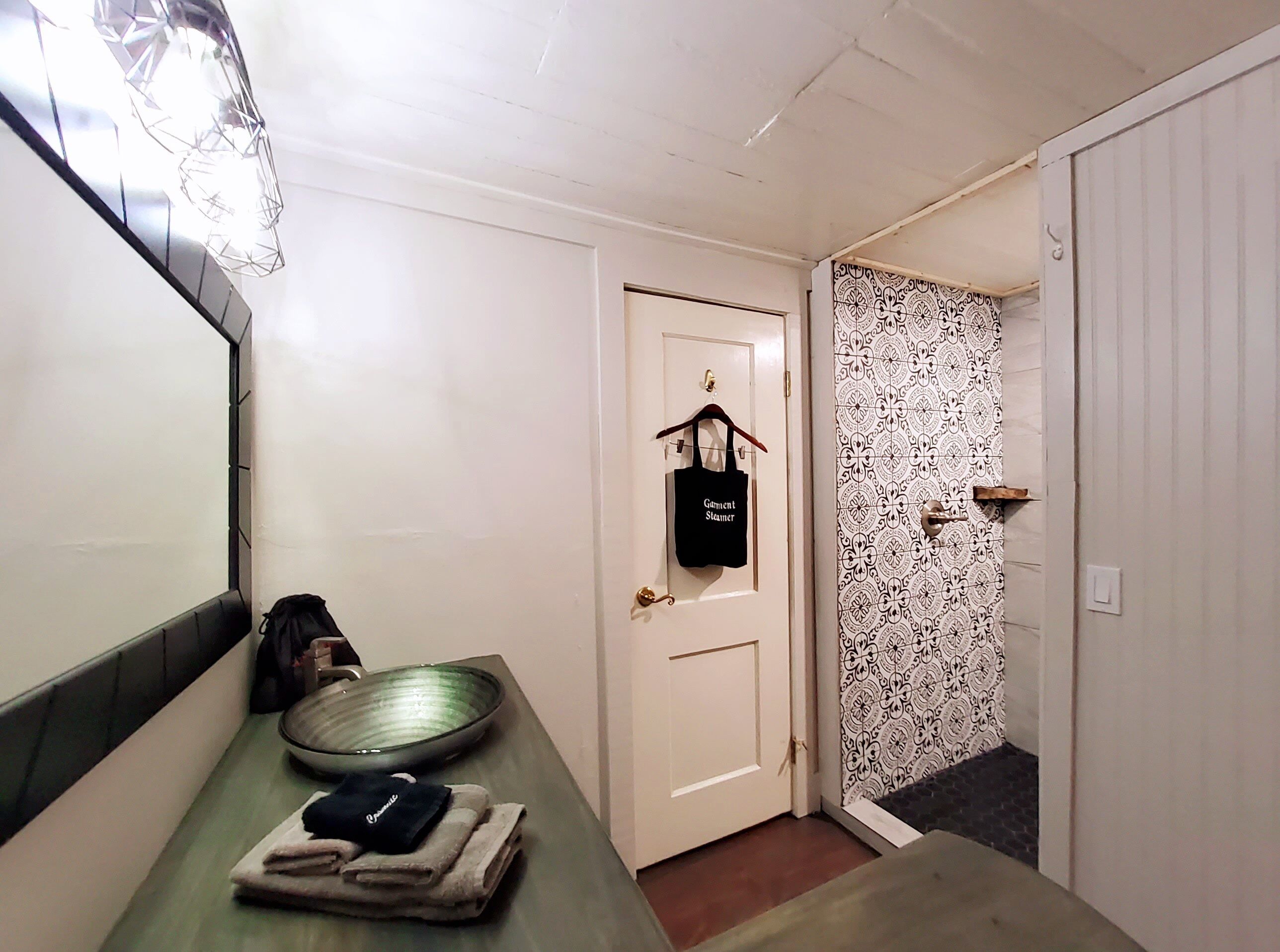 Un couloir avec un miroir, un bol, une serviette, un sac suspendu et un mur orné de motifs.