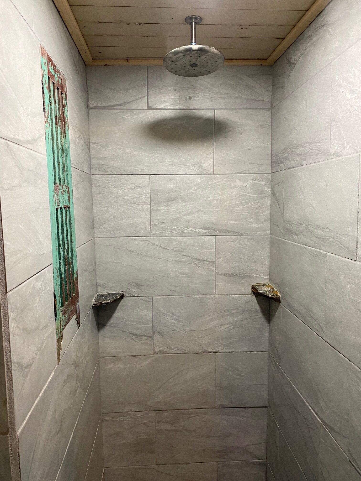 A shower with a handheld showerhead, tiled walls, and a wooden ceiling.