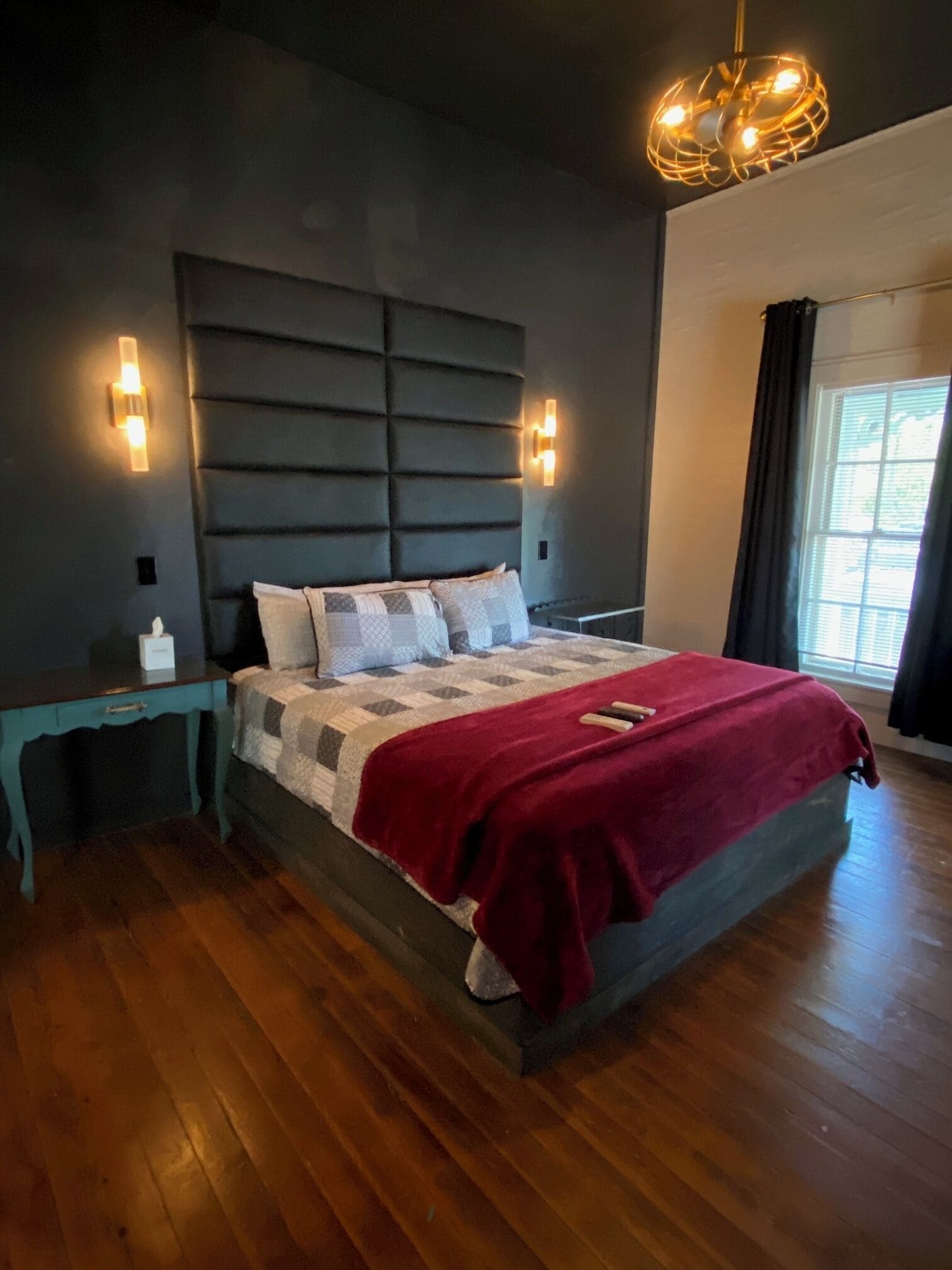 Une chambre à coucher avec un grand lit, une tête de lit sombre, des lampes de chevet, une table de chevet et une fenêtre avec des rideaux.