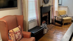 Un salon avec un grand fauteuil, une cheminée, une horloge et un téléviseur.