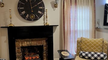 A living room with a fireplace, a large wall clock, and a patterned armchair.