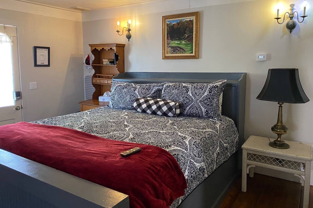 A bedroom with a bed, a nightstand, a lamp, a painting, and a fire exit plan sign.