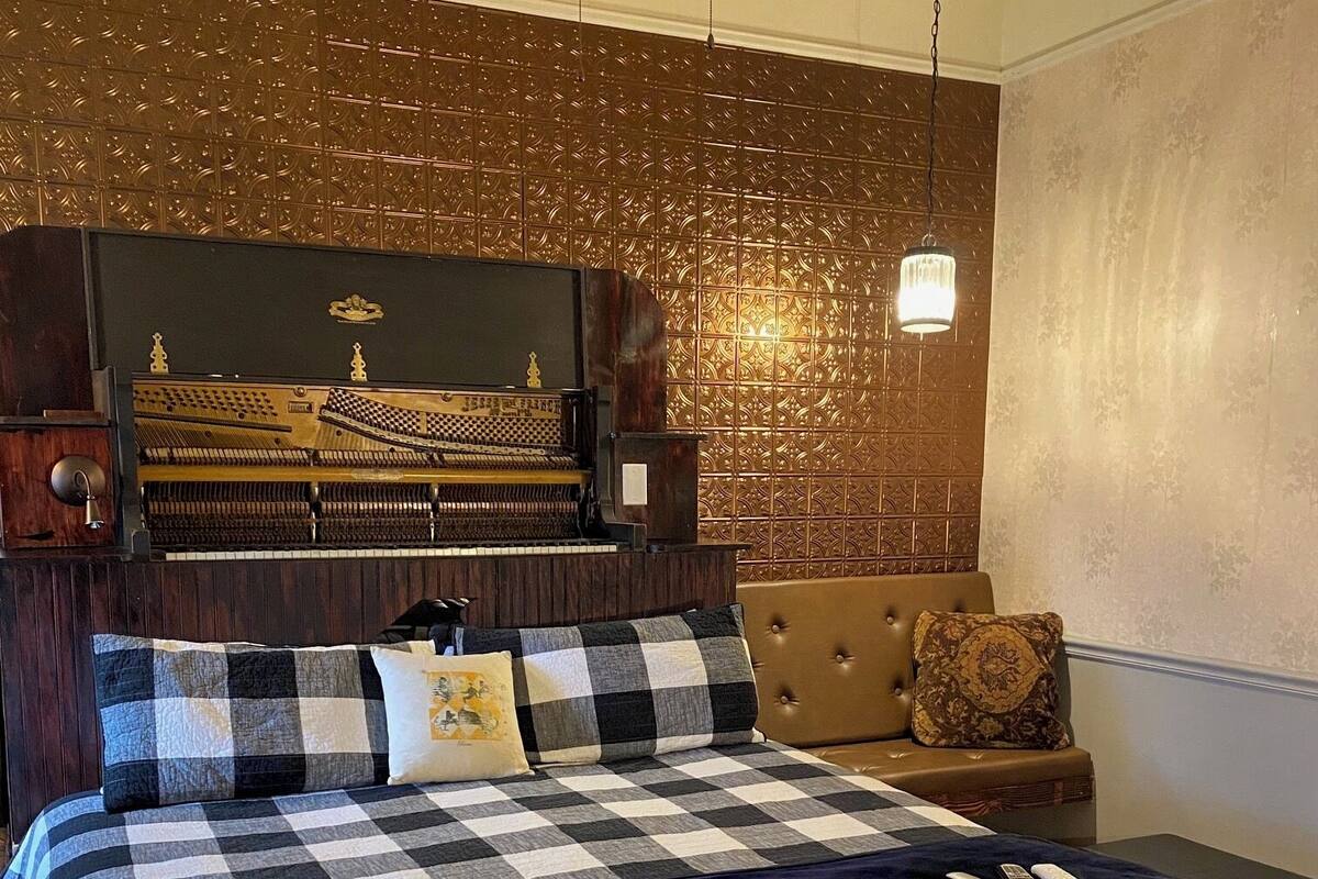 A bedroom with a large bed, a wooden headboard, a built-in piano, and a small table with a lamp.