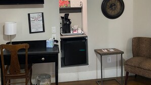 Une pièce de taille modeste comprenant un bureau, une chaise, un petit réfrigérateur, une machine à café, une horloge et un canapé.