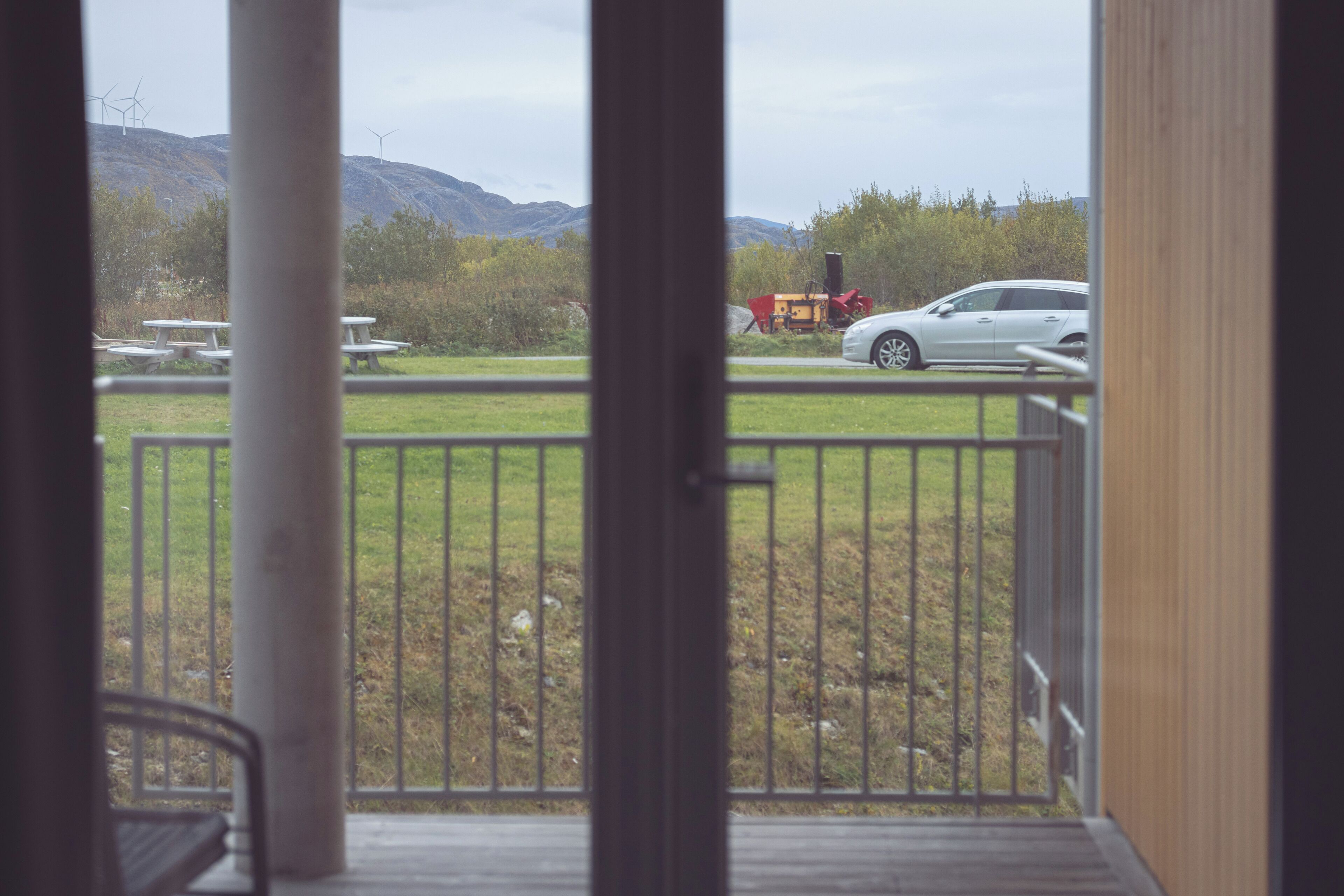 A view from a balcony with a metal railing, overlooking a grassy area with picnic tables and a parked car.
