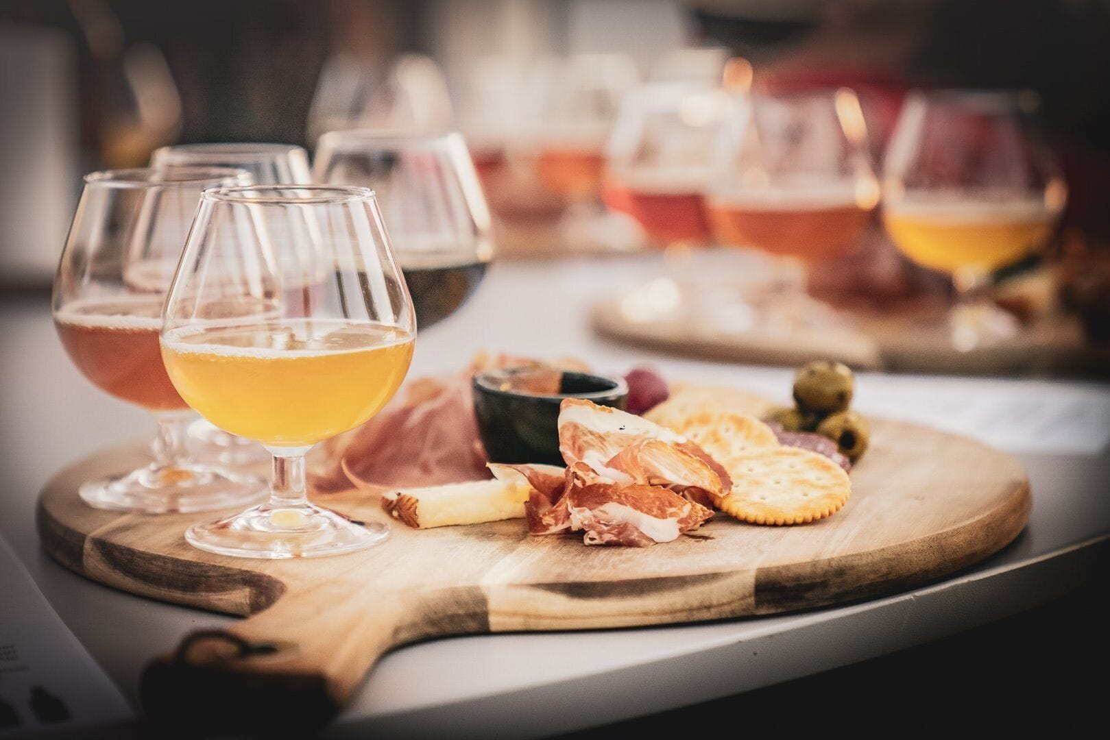 A wooden board with glasses of beer, cheese, and crackers.