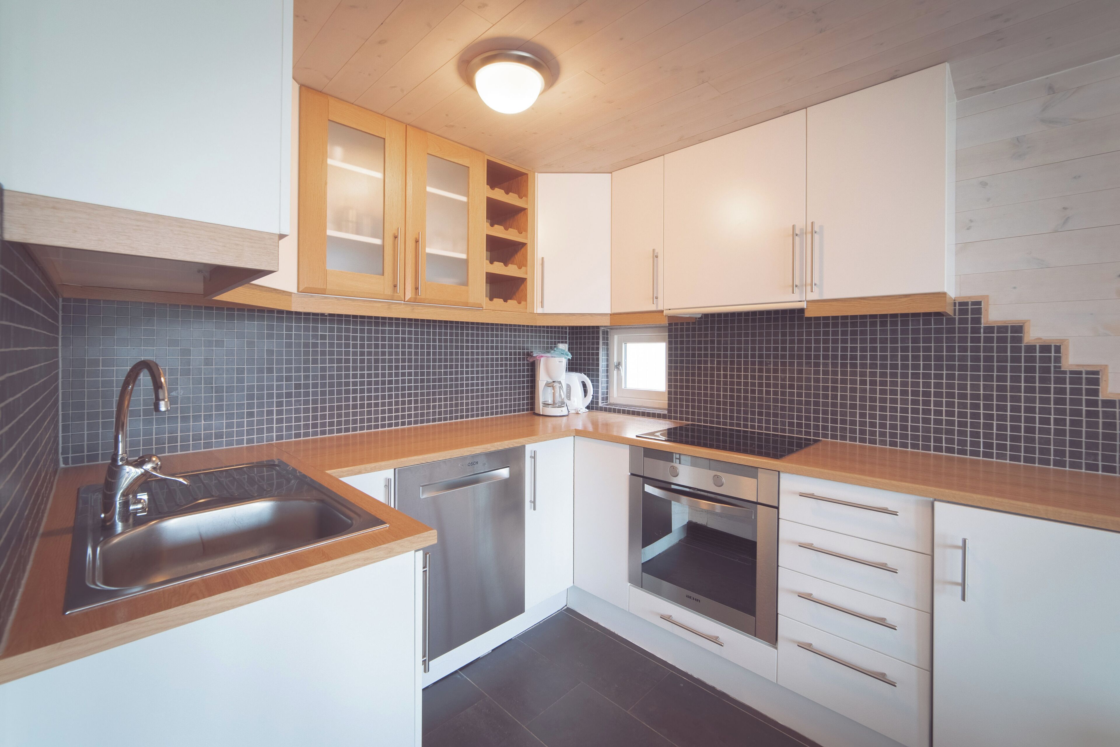 Een moderne keuken met een RVS spoelbak, een houten aanrechtblad, witte kasten en een betegelde achterwand.