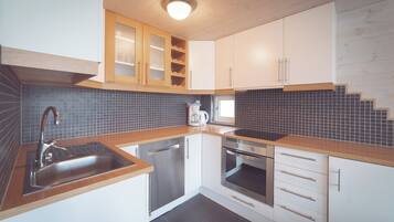 Een moderne keuken met een RVS spoelbak, een houten aanrechtblad, witte kasten en een betegelde achterwand.