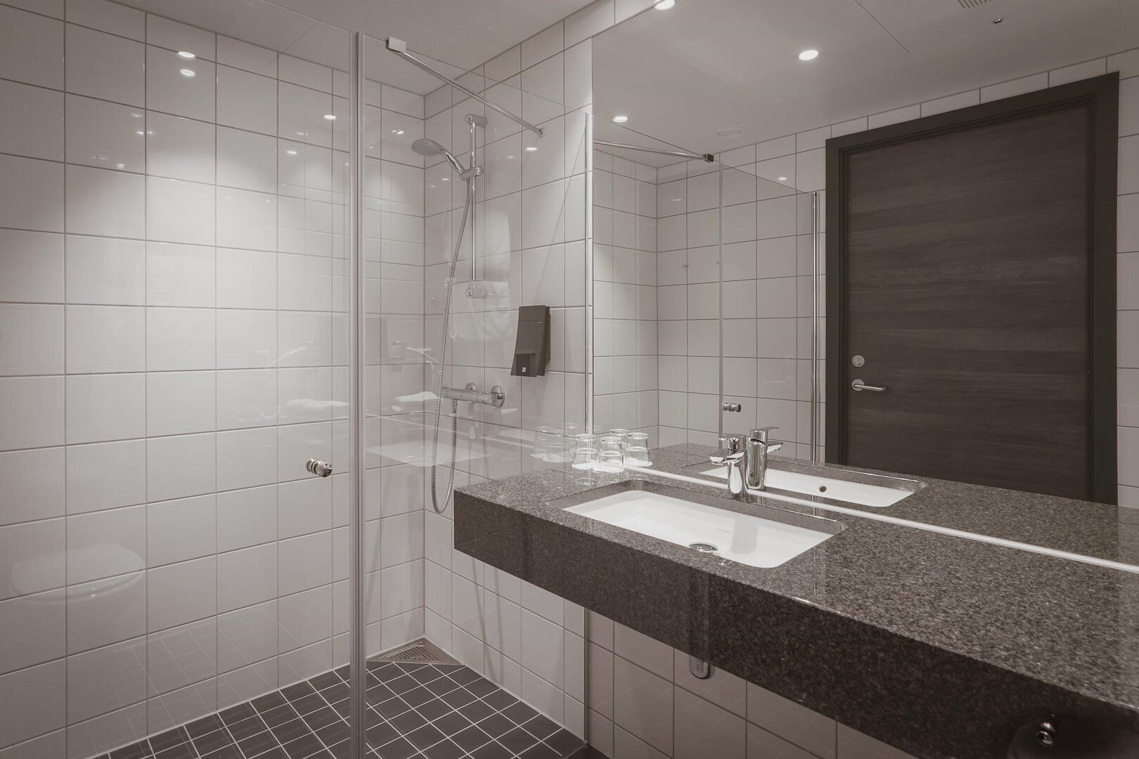 A modern bathroom with a glass-enclosed shower, a large mirror, and a granite countertop.