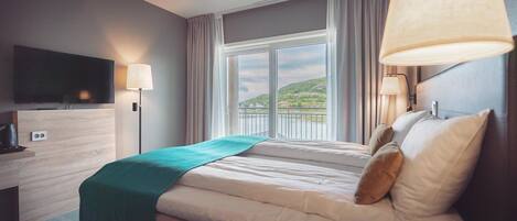 Habitación de hotel con cama, televisión, escritorio y ventana con vistas a las colinas.