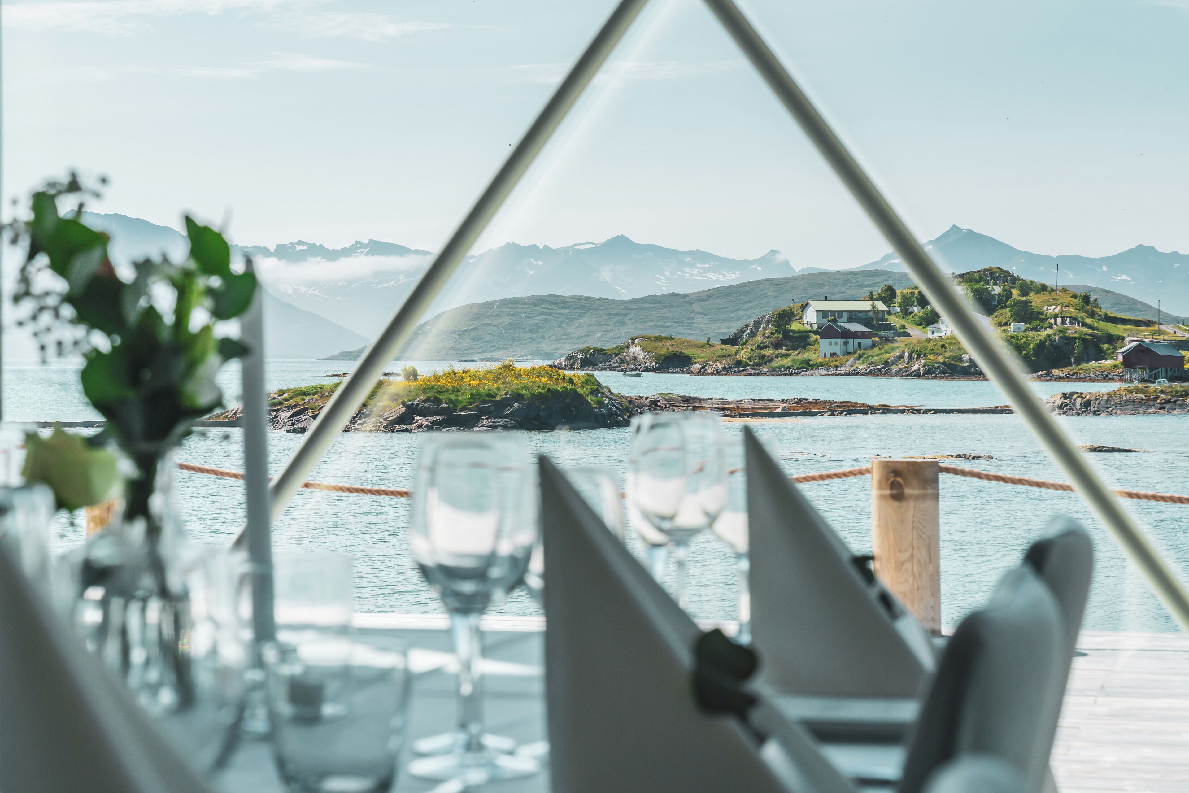 A table set for dining with a view of a coastal landscape, including mountains and a body of water.