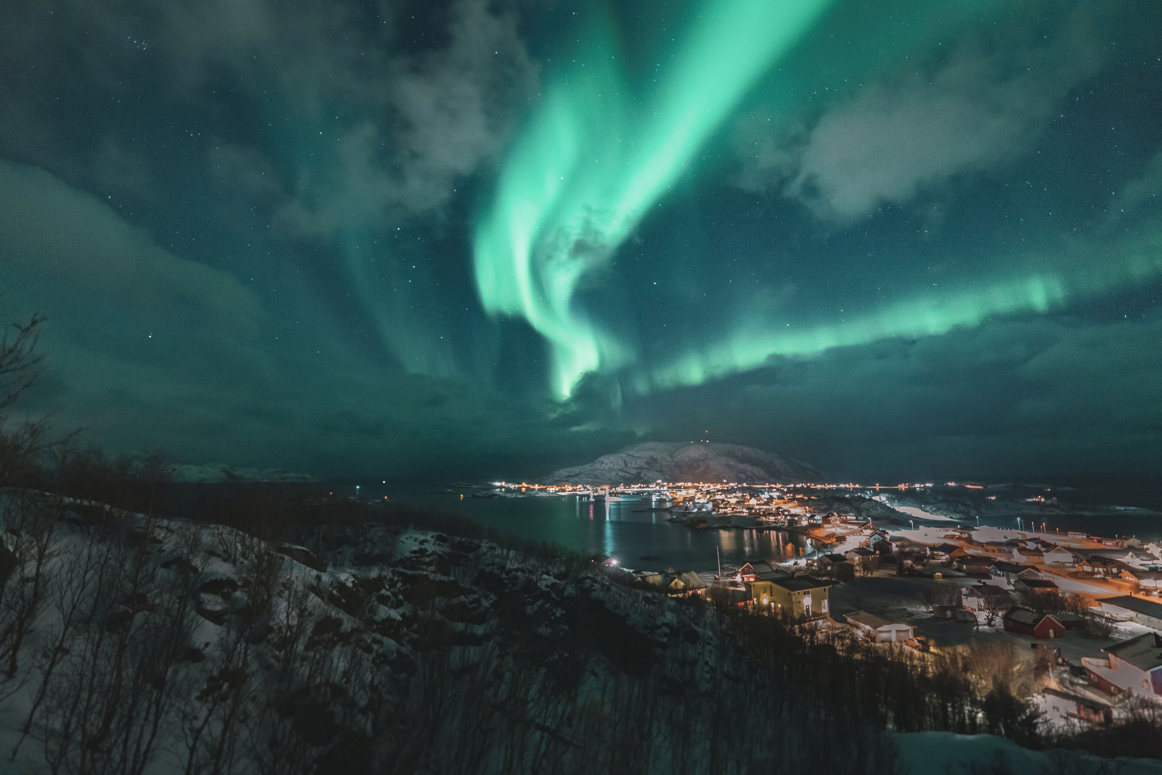 Un borgo costiero con vista sull'aurora boreale sul mare e una montagna all'orizzonte.