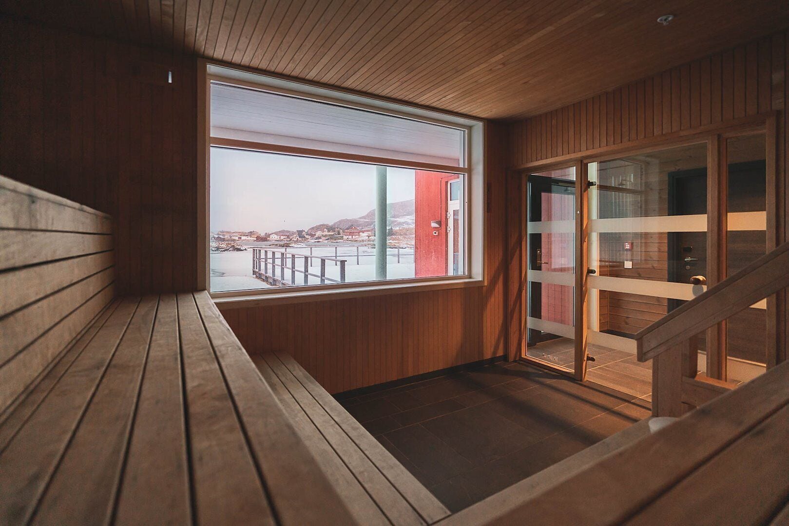 A wooden interior with a large window overlooking a dock and buildings.