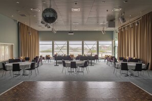 A spacious conference room with multiple tables and chairs, large windows offering a view of the outdoors, and a disco ball on the ceiling.